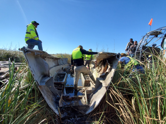A crew at work removing a damaged vessel from a marsh.