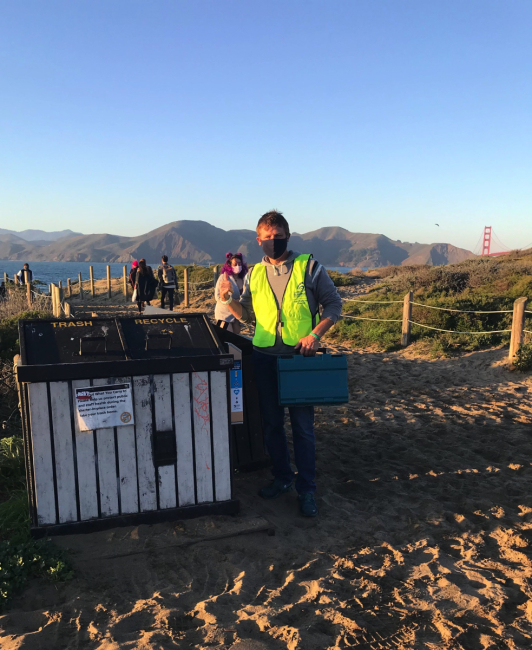A volunteer standing next to a beachside buttcan.