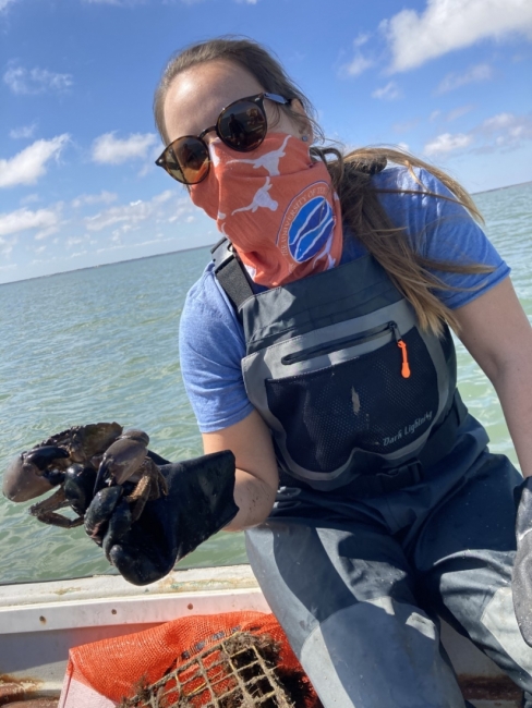 A woman with a cloth mask sitting in a boat holds up a crab recovered from an abandoned trap.