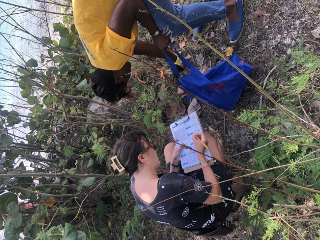 A volunteer picking up marine debris along a shoreline while another volunteer marks the type of debris on a datasheet.