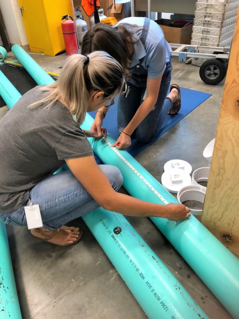 Two people measure a pipe.
