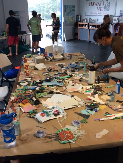 Students bend over a table covered with art supplies, work to create an education product about the new filling stations.