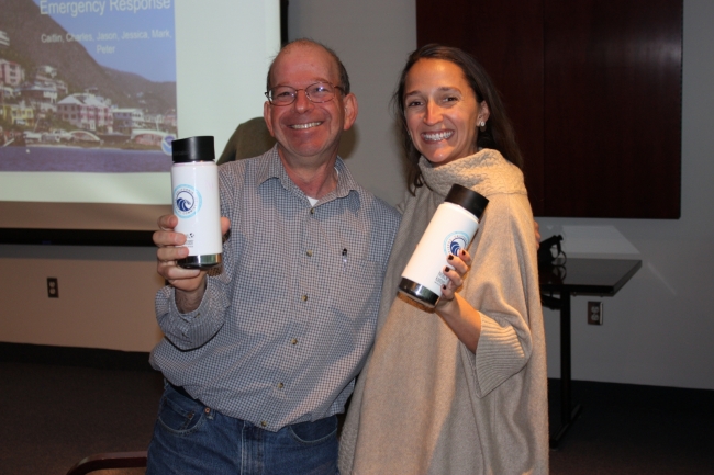 Two people smile side by side while holding up reusable water bottles. 