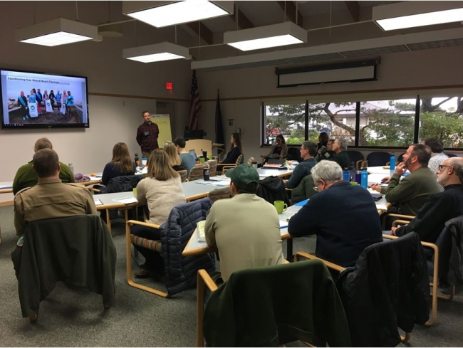 Participants sit a tables watching a presentation.