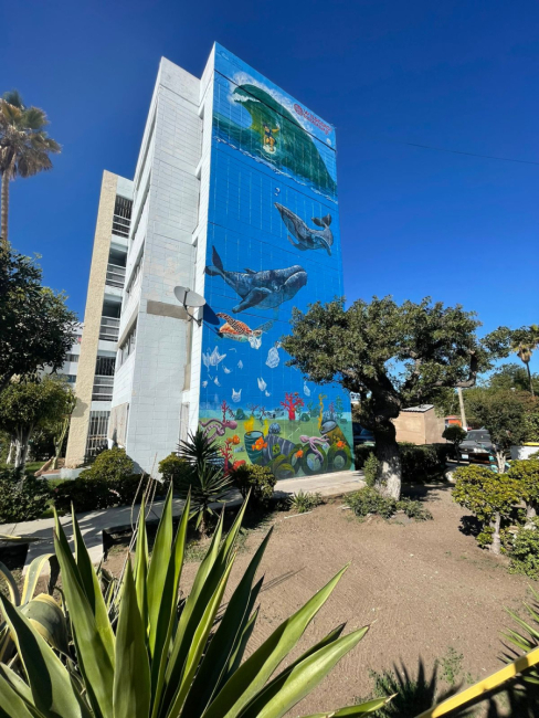 An apartment building with a marine debris mural painted on its side depicting whales and plastic bags. 