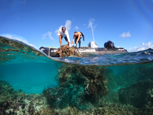 Two people pulling a large net out of the water and onto a boat.