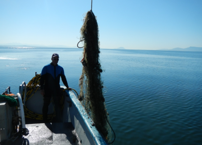 A person on a boat standing next to a derelict fishing net.