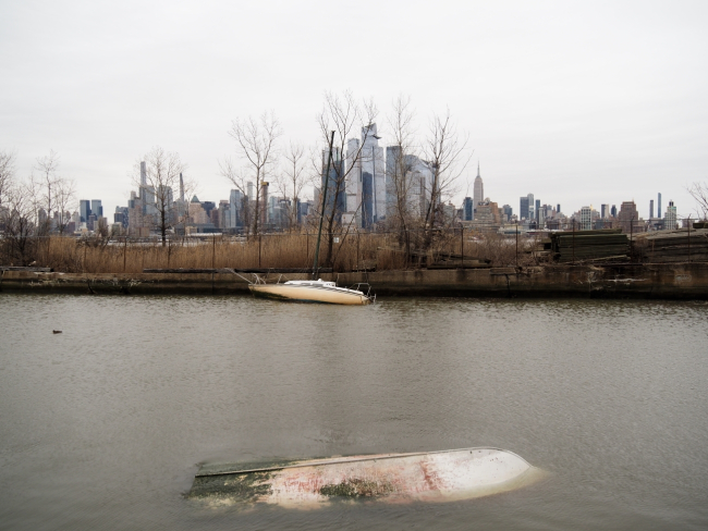 A partially and completely submerged pair of vessels in a cove with a big city skyline in the distance.