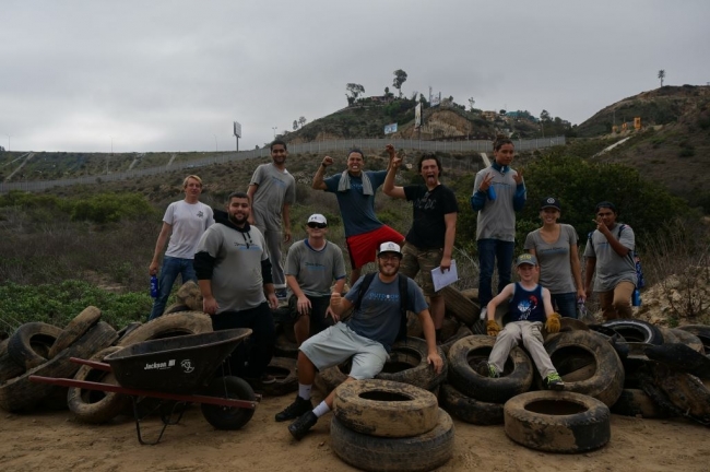 11 people smile for a picture around a large pile of collected tires. 
