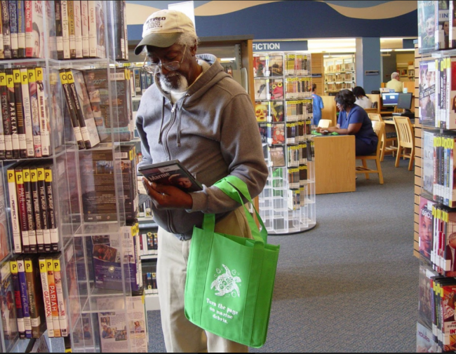 A man with a reusable bag browsing in the library.