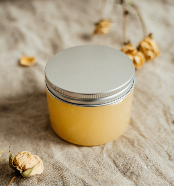 A reusable jar containing a homemade scrub on a  tablecloth surrounded by small yellow flowers.
