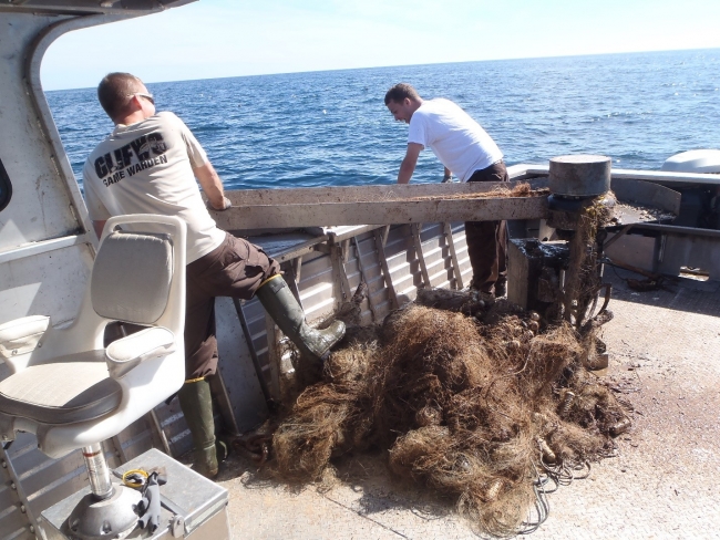 Two people hauling a derelict net onto a boat.