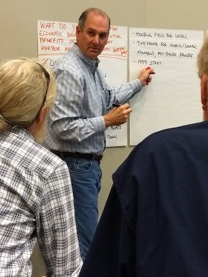 A person stands near a wall while pointing to a notes written on large, poster paper.