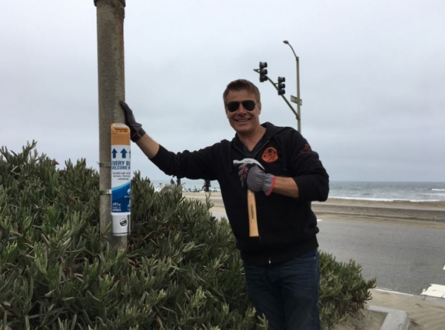A person stands near a newly installed cigarette butt container smiling for a picture.
