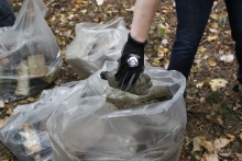 A person putting a collected plastic bottle into a bag of other debris.