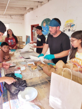 A group of children and adults standing around a table as they unpack take out food orders.