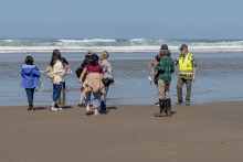  A group of young students holding a 5-meter rope stand on a sandy beach and look out into the waves.