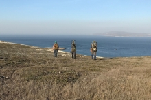 Three people hiking down a grassy hillside toward the ocean.