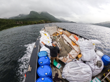 A person pointing to a mountainous shoreline aboard a moving vessel that is loaded with marine debris items that was removed during a cleanup.