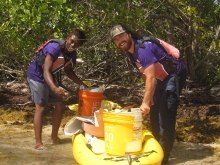 Two guys in mangroves, leaning over a kayak with collected debris.