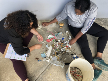 Two volunteers sorting through miscellaneous marine debris items and classifying types on a datasheet.