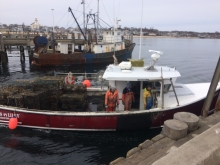 A boat in harbor with a pile of derelict traps and three people on board.