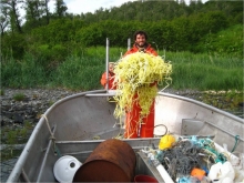 A man dressed in all orange stands in a boat holding a pile of yellow rope.
