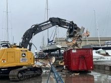 An excavator breaking down a derelict vessel and placing it into a dumpster.