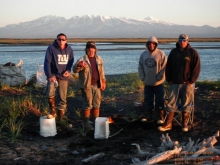 Four men in front of a river with a snow-capped mountain in the background. 