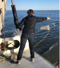 A person stands on a boat deploying a net to collect microplastics.
