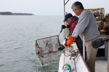 Two people pull up derelict crab traps on the side of a boat.