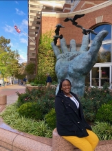 A young person sits in front of a large statue that is shaped like a hand.