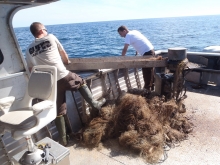 Two people hauling a derelict net into a boat.
