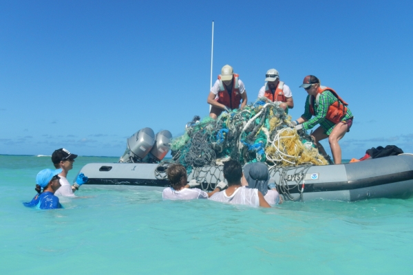 People in a small boat and in the water hauling derelict nets into the boat.