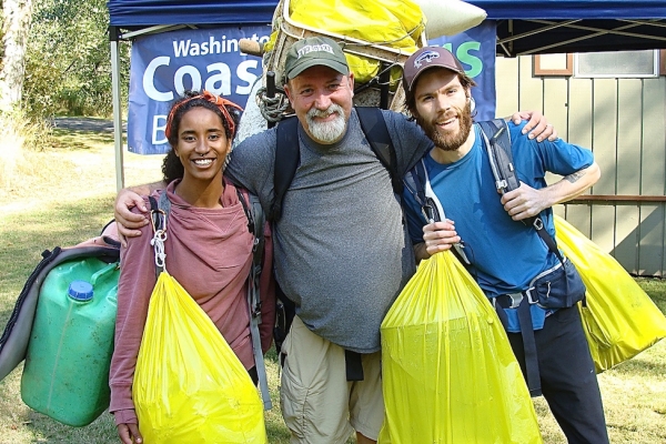 Three people holding bags of debris.