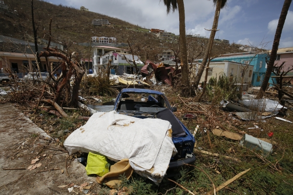 In the foreground a car and mattress are surrounded by debris and heavily damaged homes.