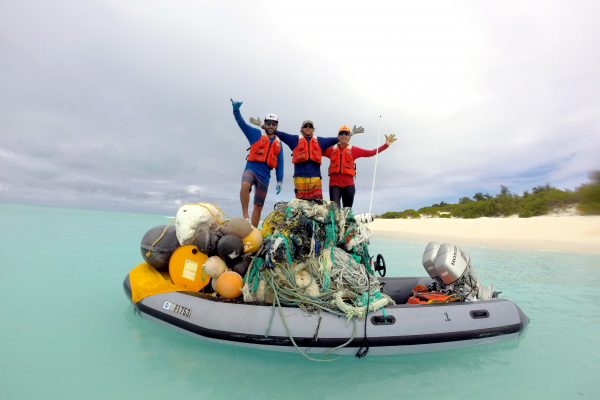 Members of the marine debris team stand proudly on top of a large pile of debris.